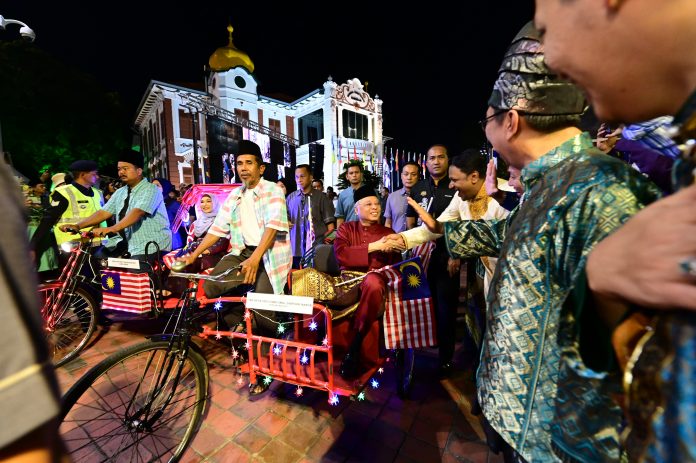 Pengayuh beca veteran Rosli Mad Zin, 63, membawa Ismai Sabri ke pentas utama Sambutan Hari Malaysia di Melaka malam ini.Foto Jabatan Penerangan
