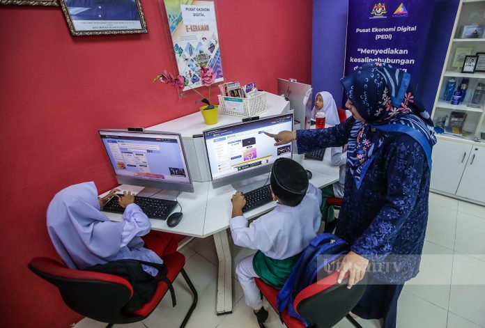 Tenaga pengajar, Nurhasni Haizan Hasmadon membantu murid-murid sekolah menggunakan komputer ketika menyertai sesi e-pembelajaran di Pusat Ekonomi Digital (PEDi) Felda Soeharto, Hulu Selangor, hari ini. GAMBAR: Abd Razak Aid